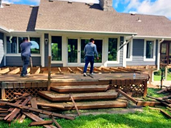 Crew tearing out an old wooden deck, boards stacked on the lawn.